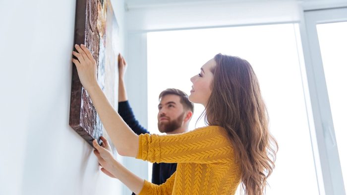 woman in yellow sweater and man with beard hanging artwork on a wall